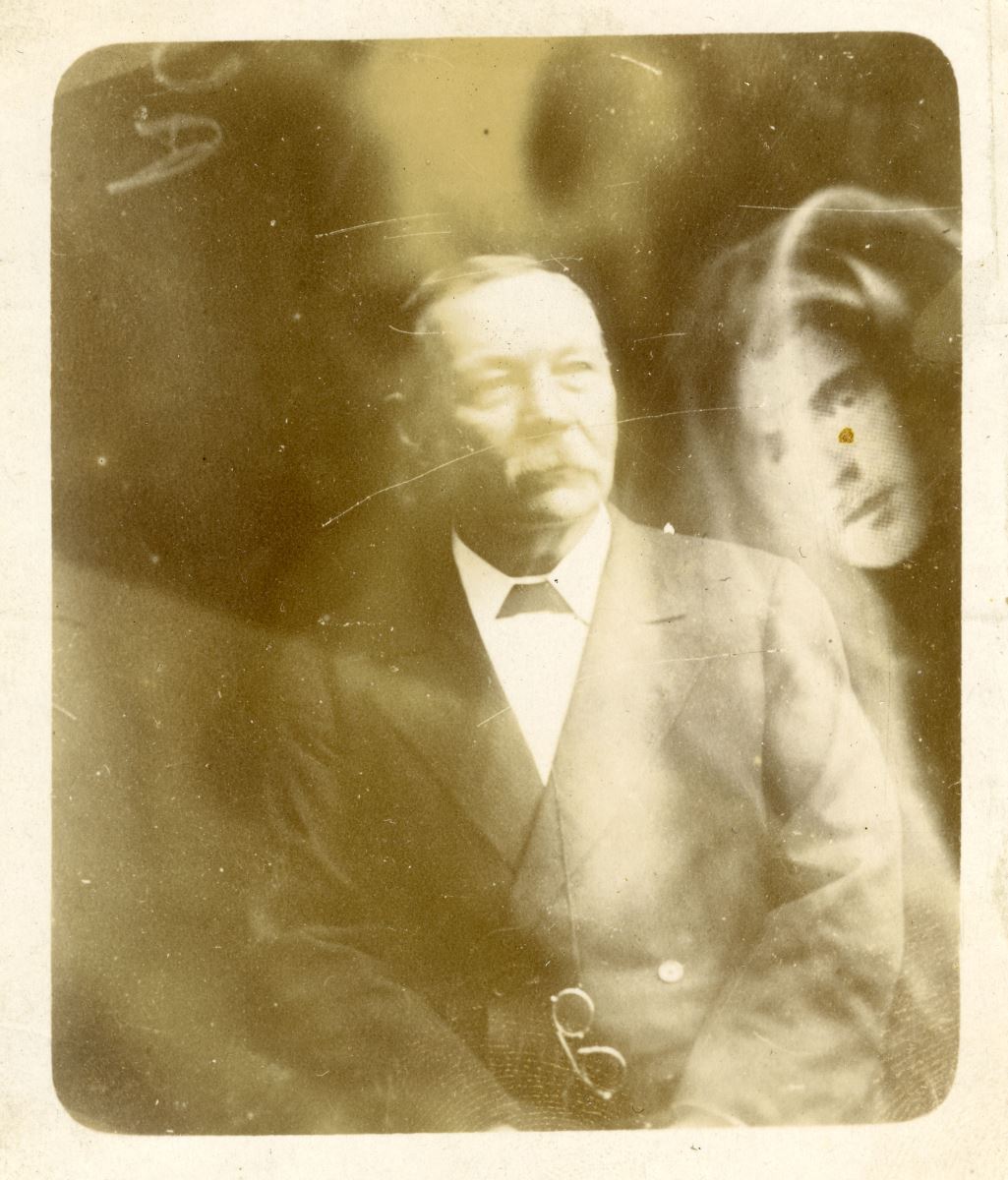 A photo of conan doyle with a ghostly face in the background
